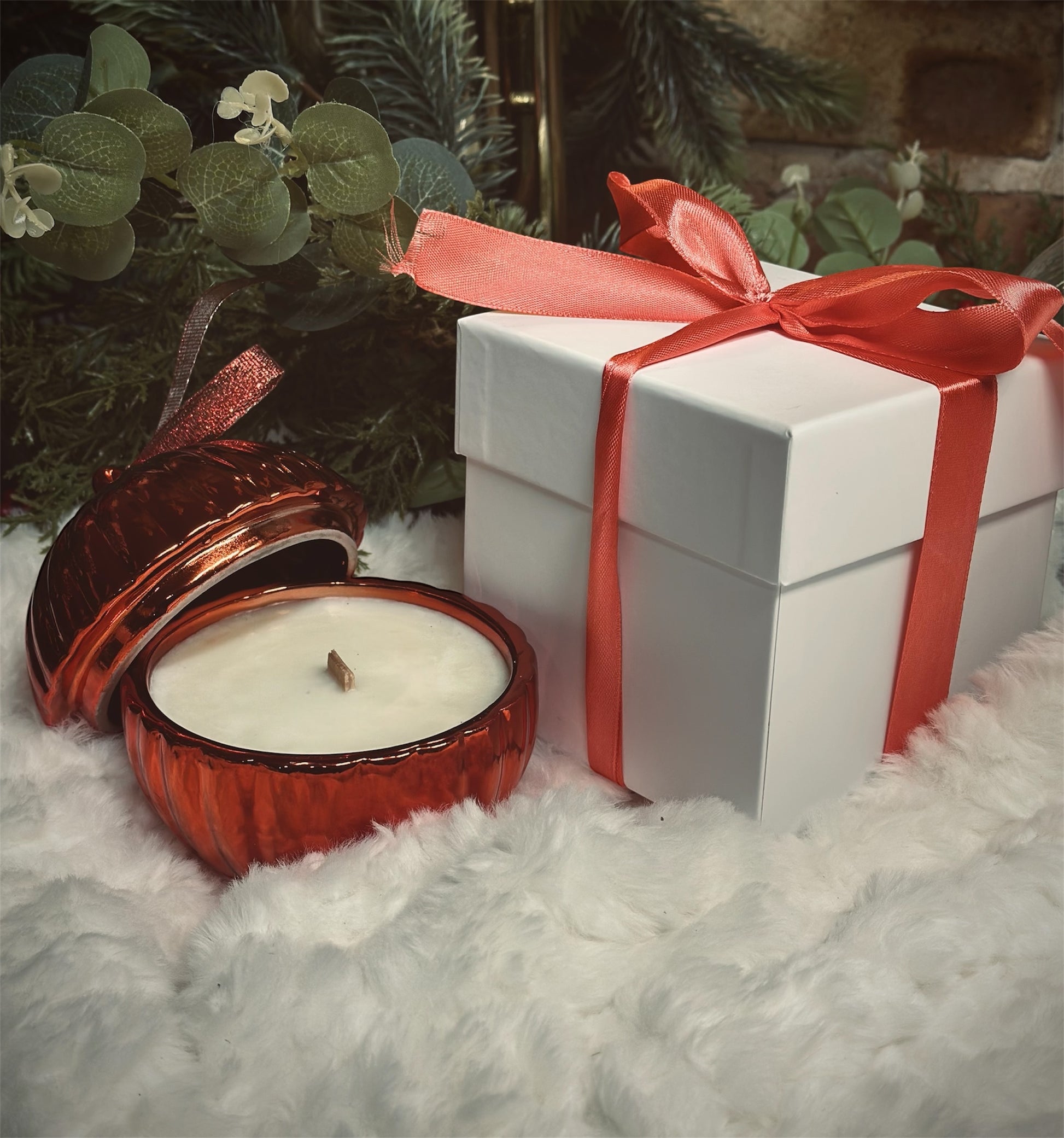 Red candle and white gift box with red ribbon on a snowy surface